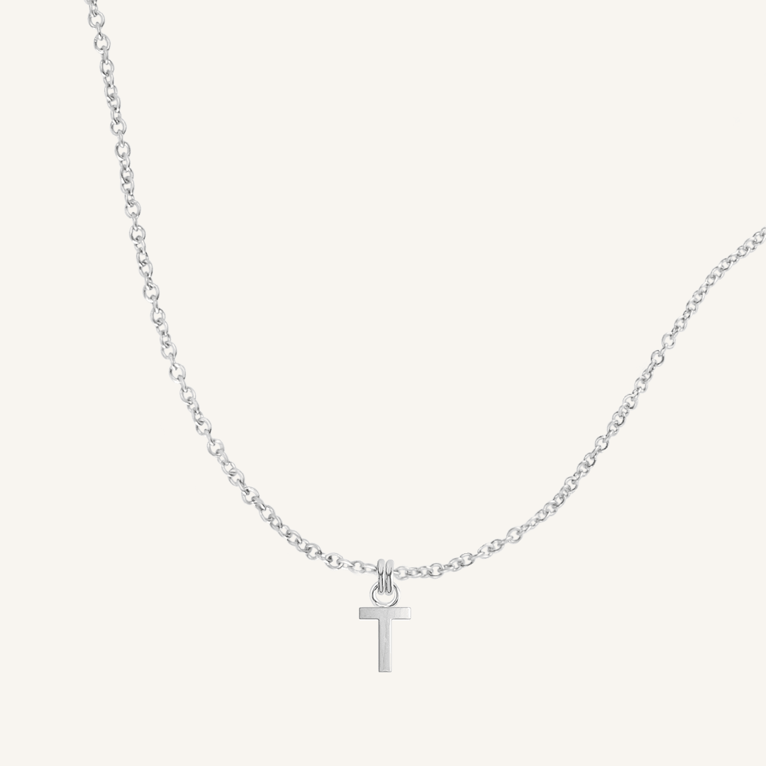 Silver necklace with a T pendant on a light gray background