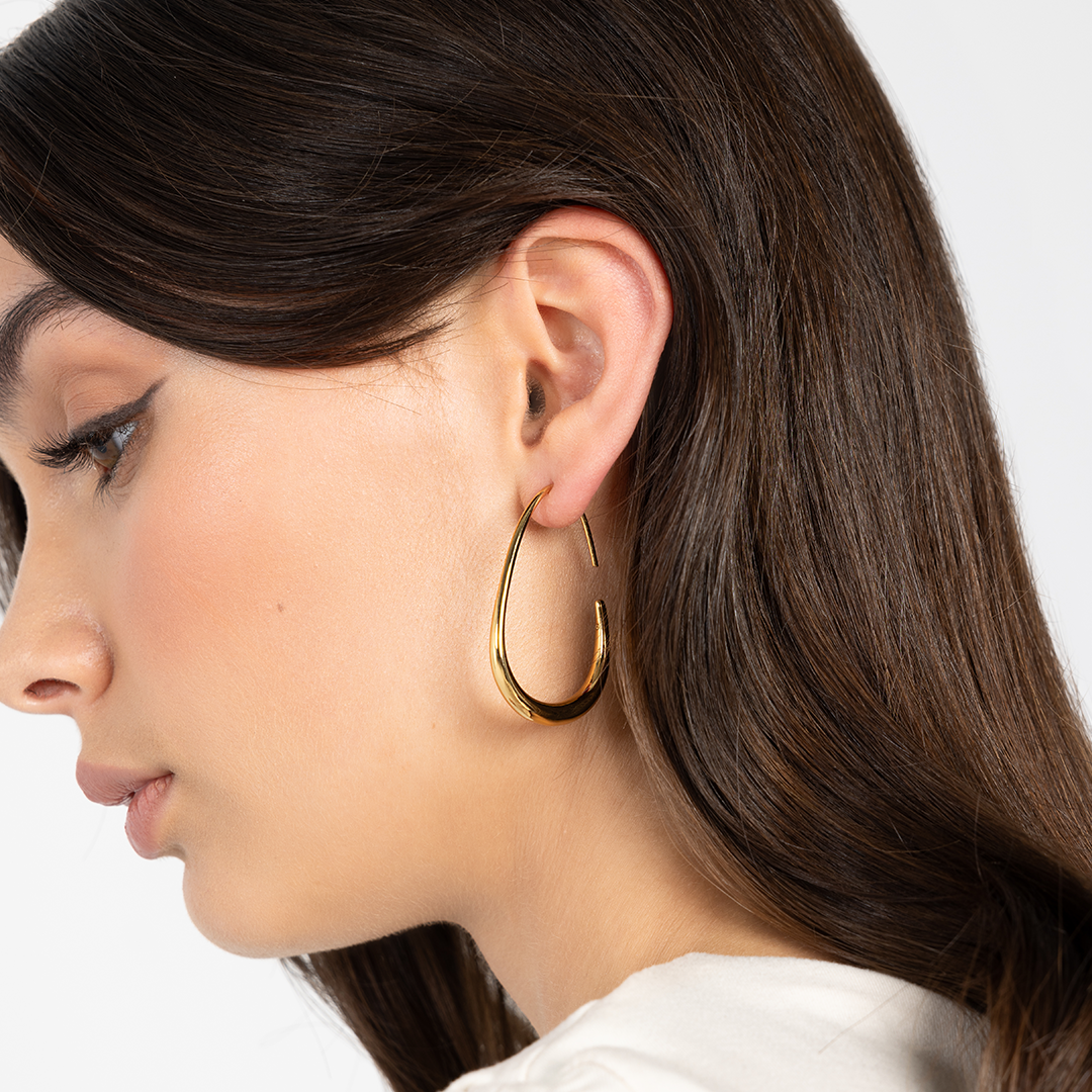 Woman wearing a gold hoop earring with a white background