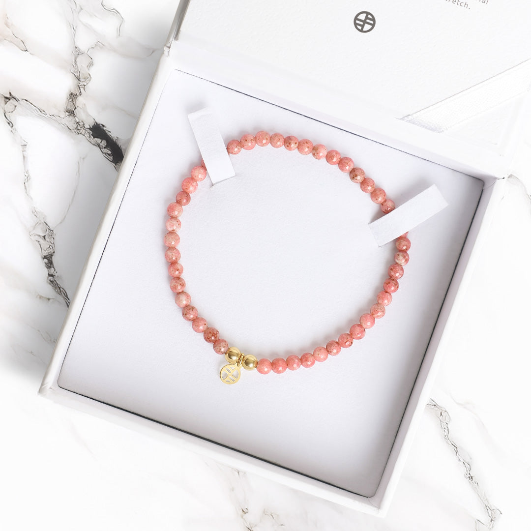 Pink beaded bracelet with a gold charm on a white marble surface