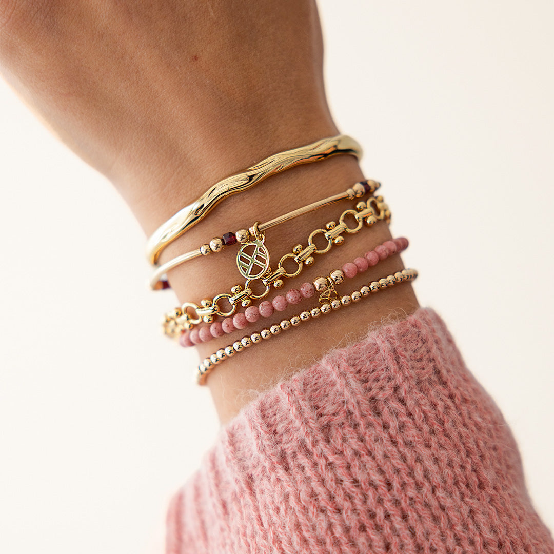 Stack of gold and pink bracelets on a wrist with a blurred background