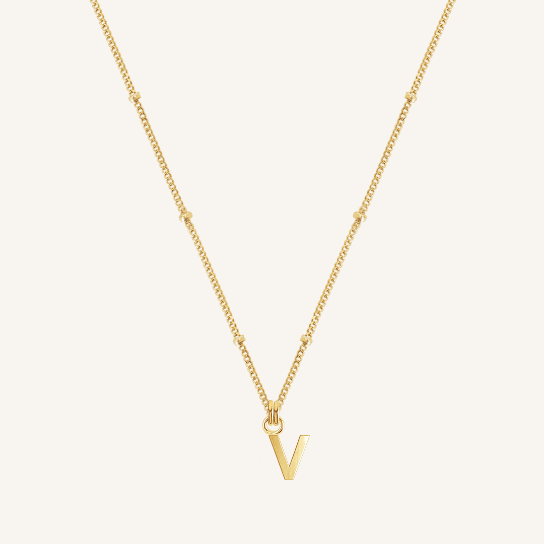 Gold necklace with a 'V' pendant on a light beige background
