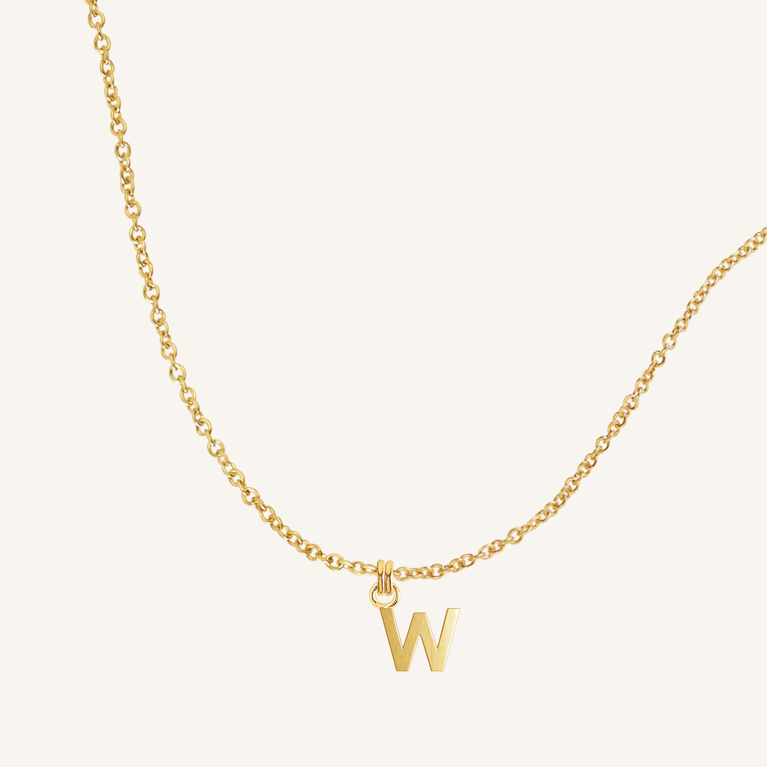 Gold necklace with a 'W' pendant on a light beige background