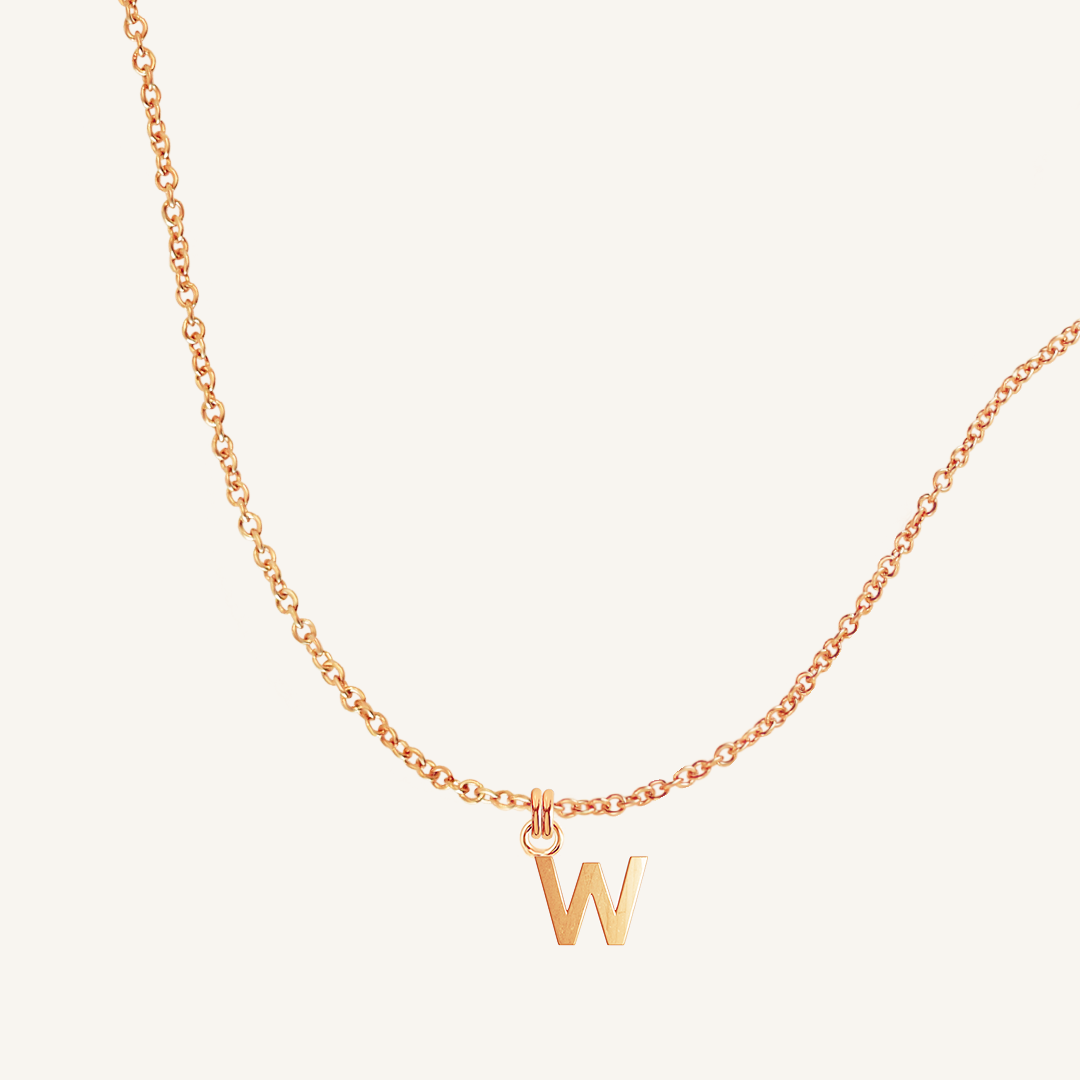 Rose gold necklace with a 'W' pendant on a light beige background
