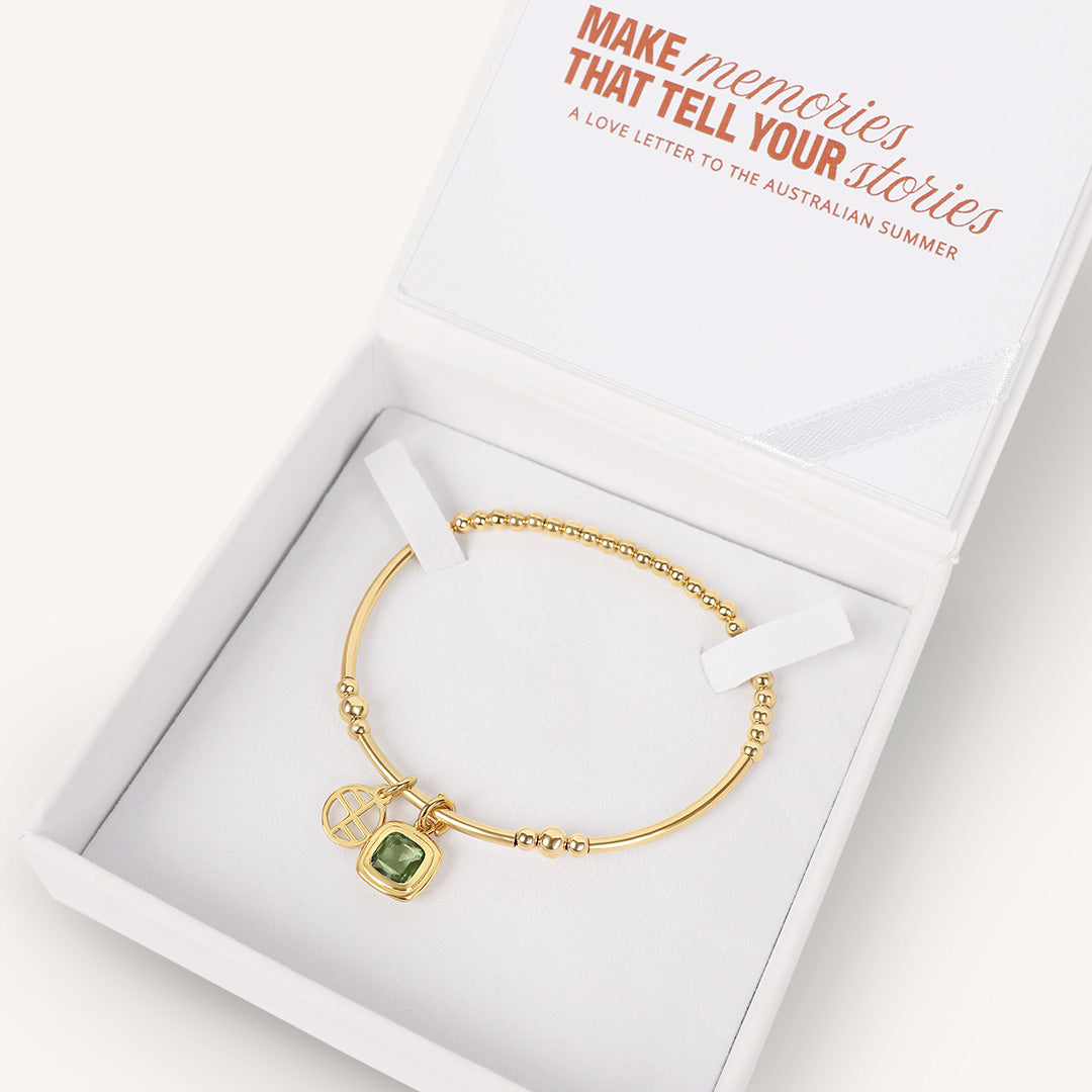 Gold bracelet with a green gemstone in a white box with text