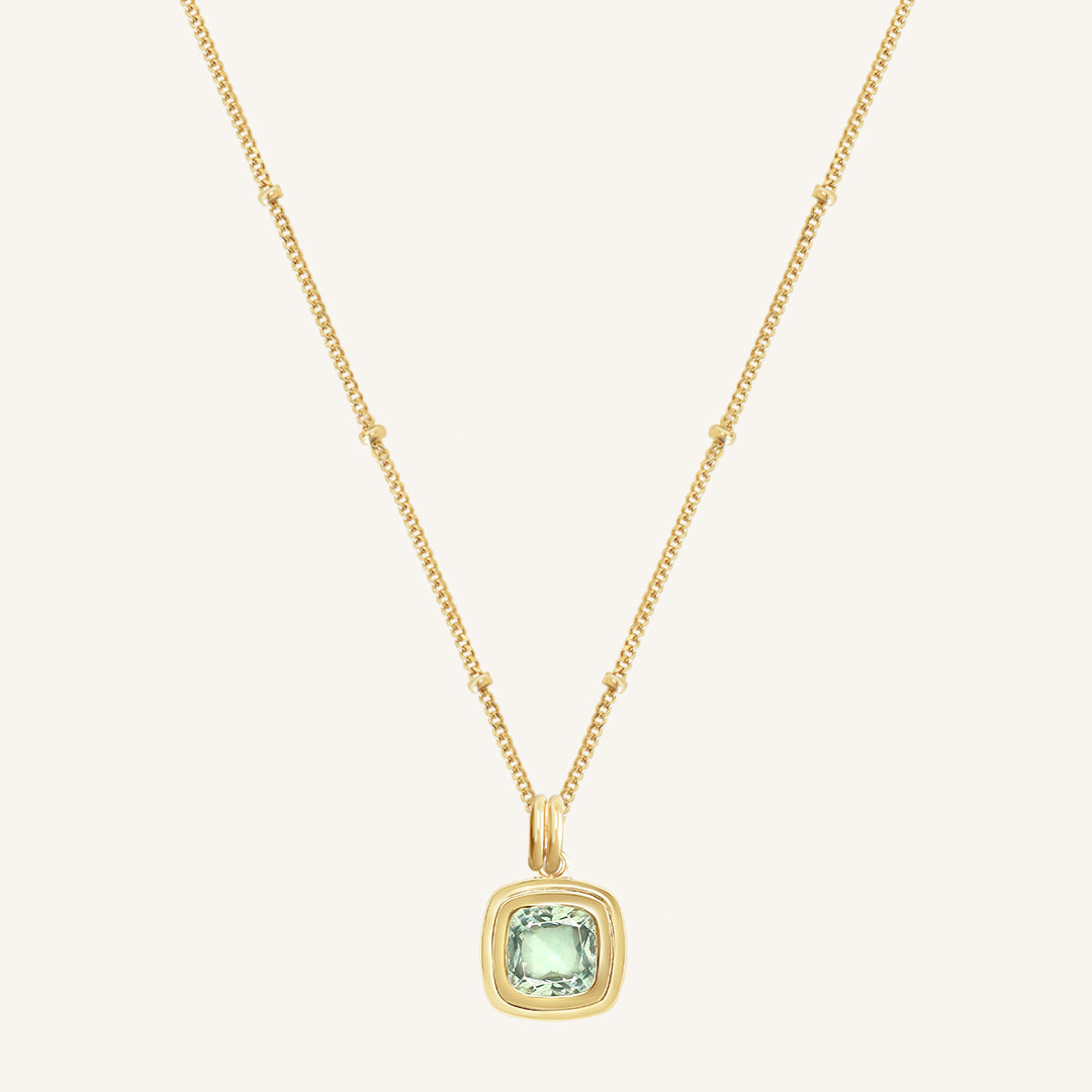 Gold necklace with a green gemstone pendant on a light beige background
