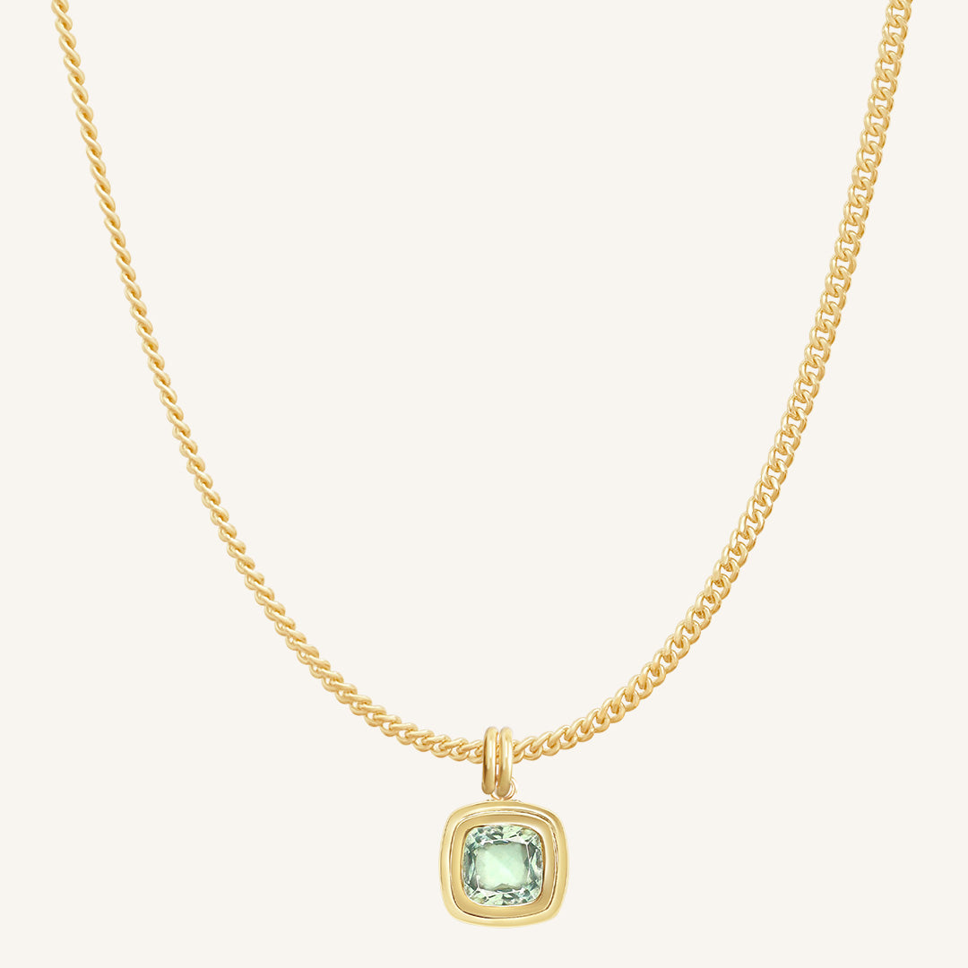 Gold necklace with a green gemstone pendant on a white background