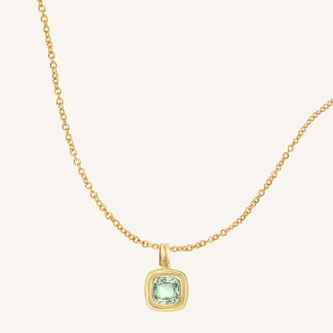 Gold necklace with a green gemstone pendant on a white background