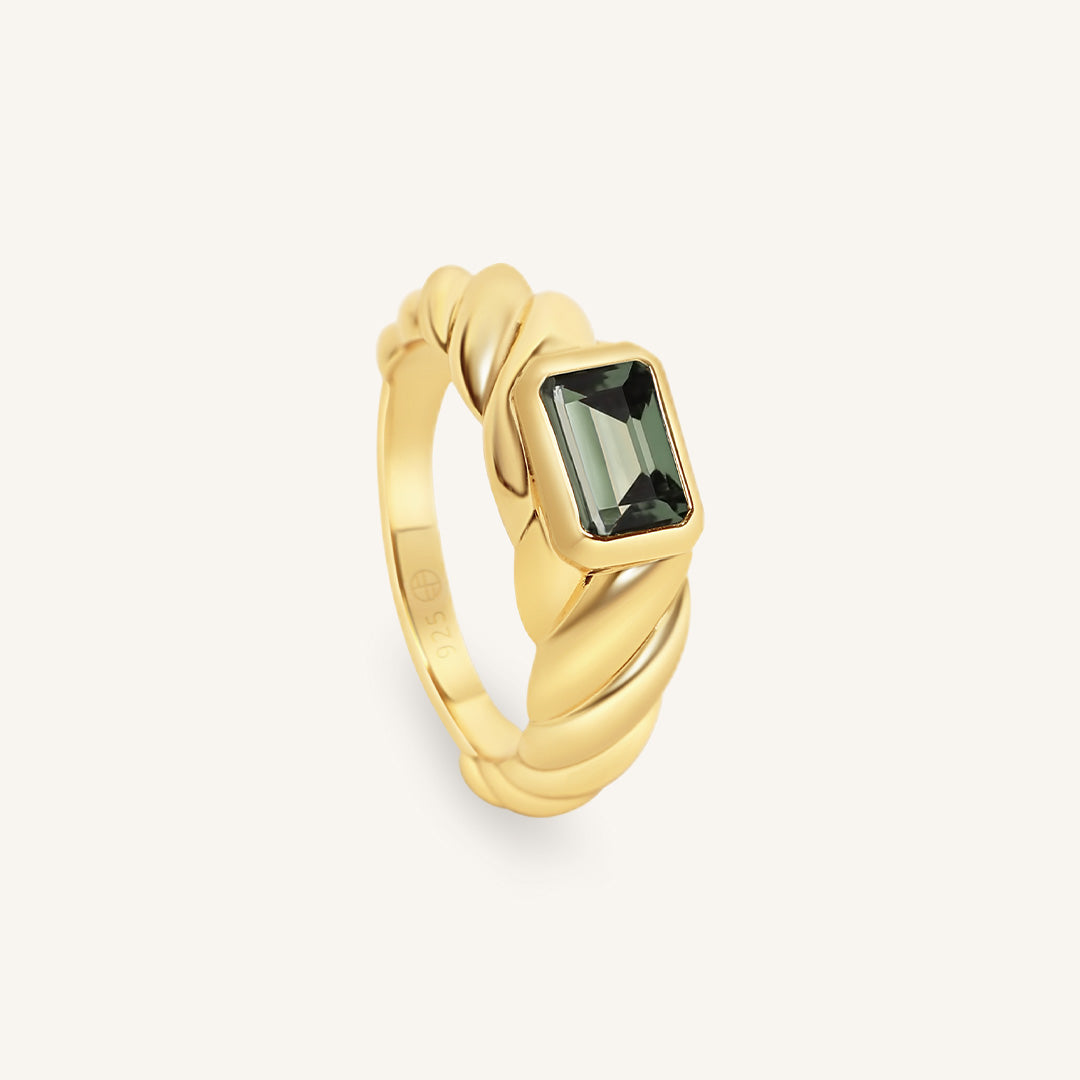 Gold ring with a green gemstone on a light gray background