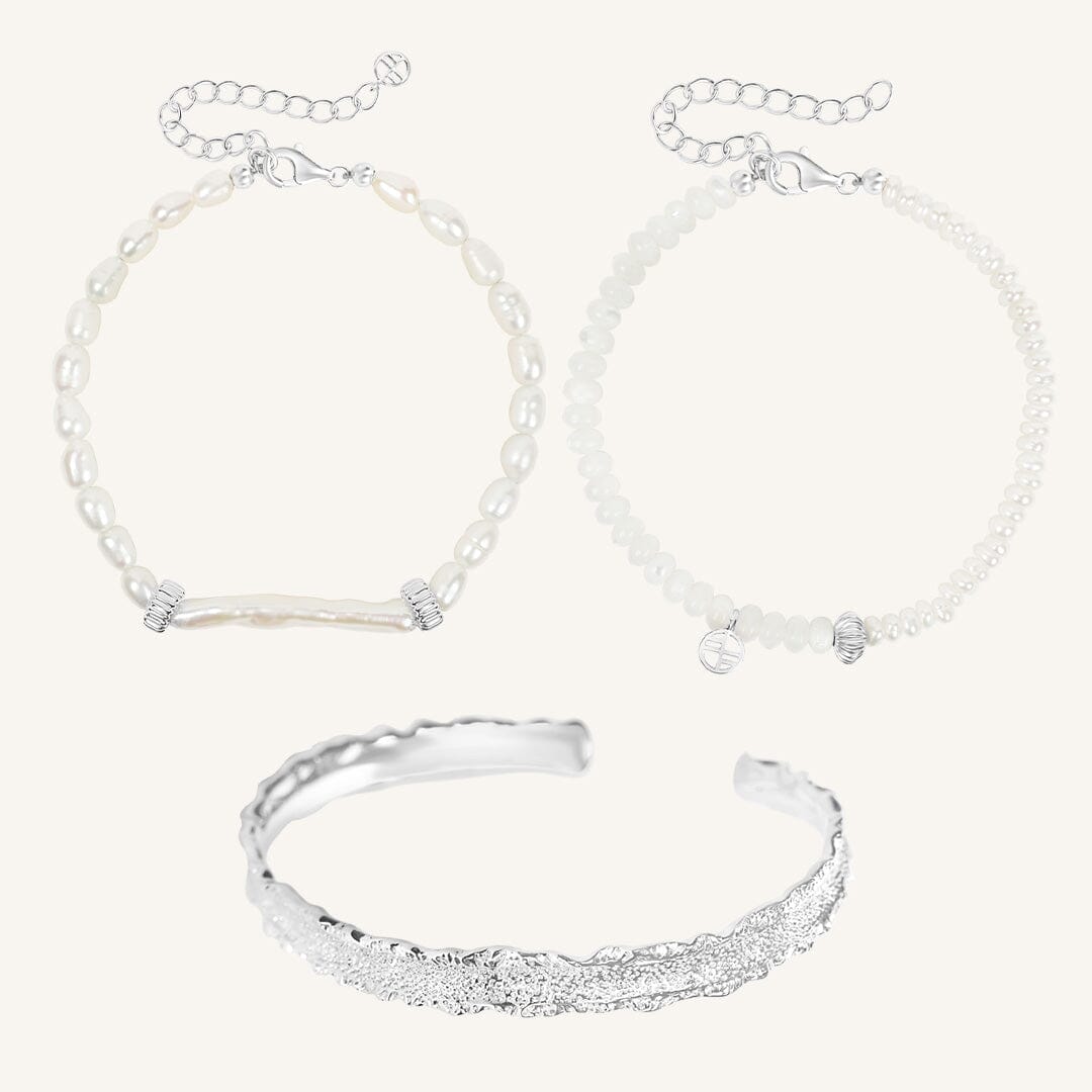 Silver bracelet and two pearl beaded bracelets on a light gray background