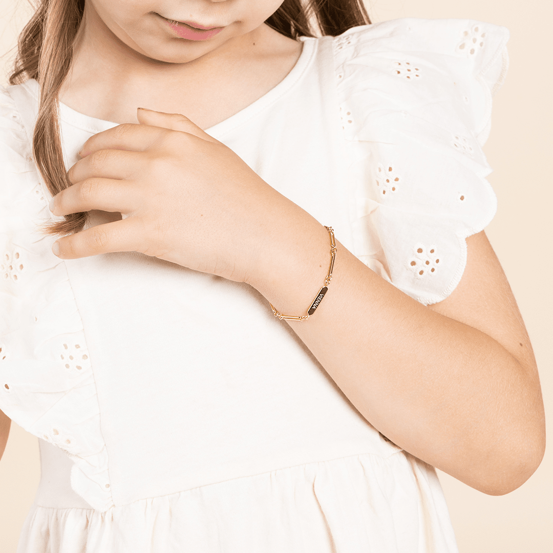 A gold-tone bracelet with a chain design and an engraving bar, worn on childs wrist