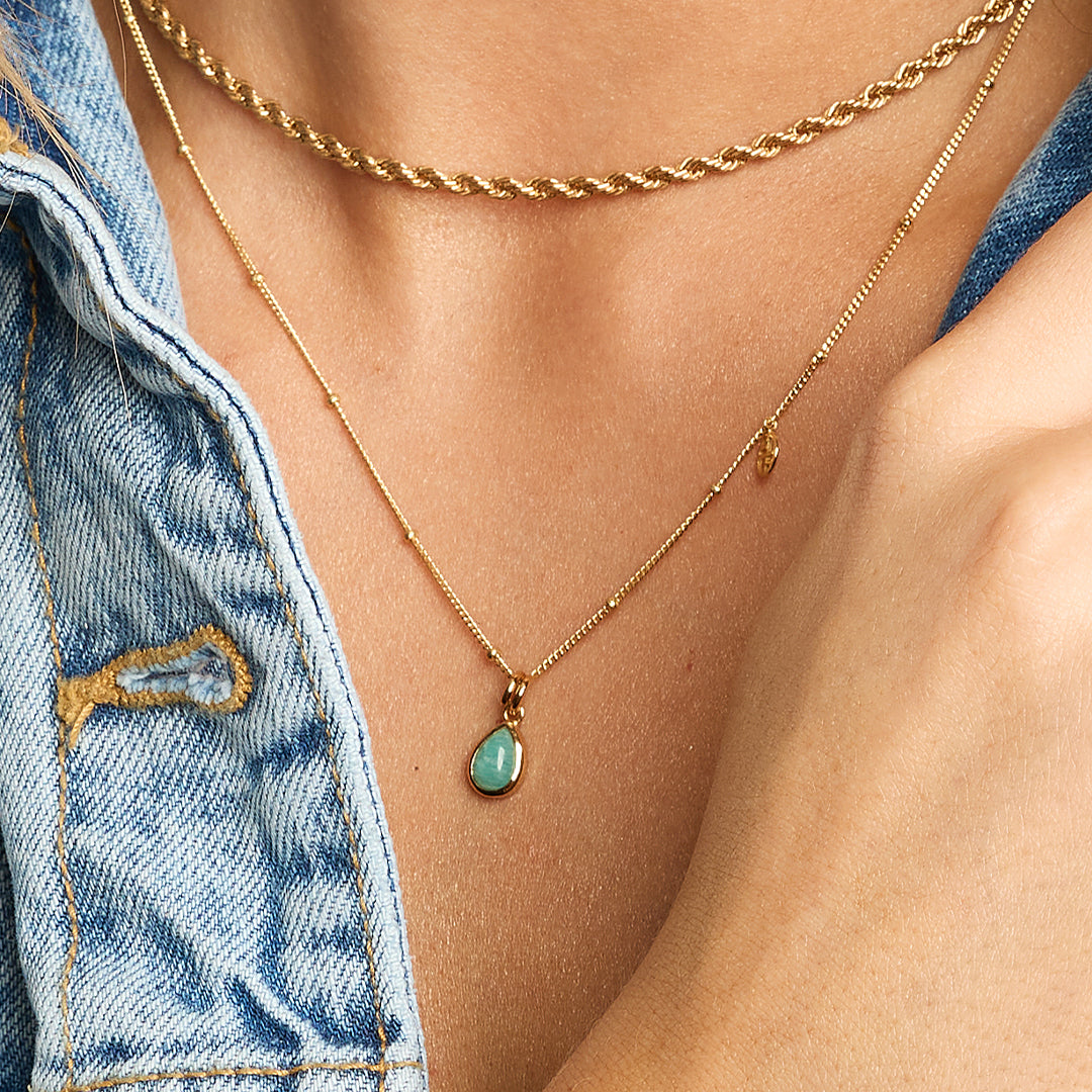 A gold charm with a teardrop-shaped amazonite stone set in a bezel on chain around the neck
