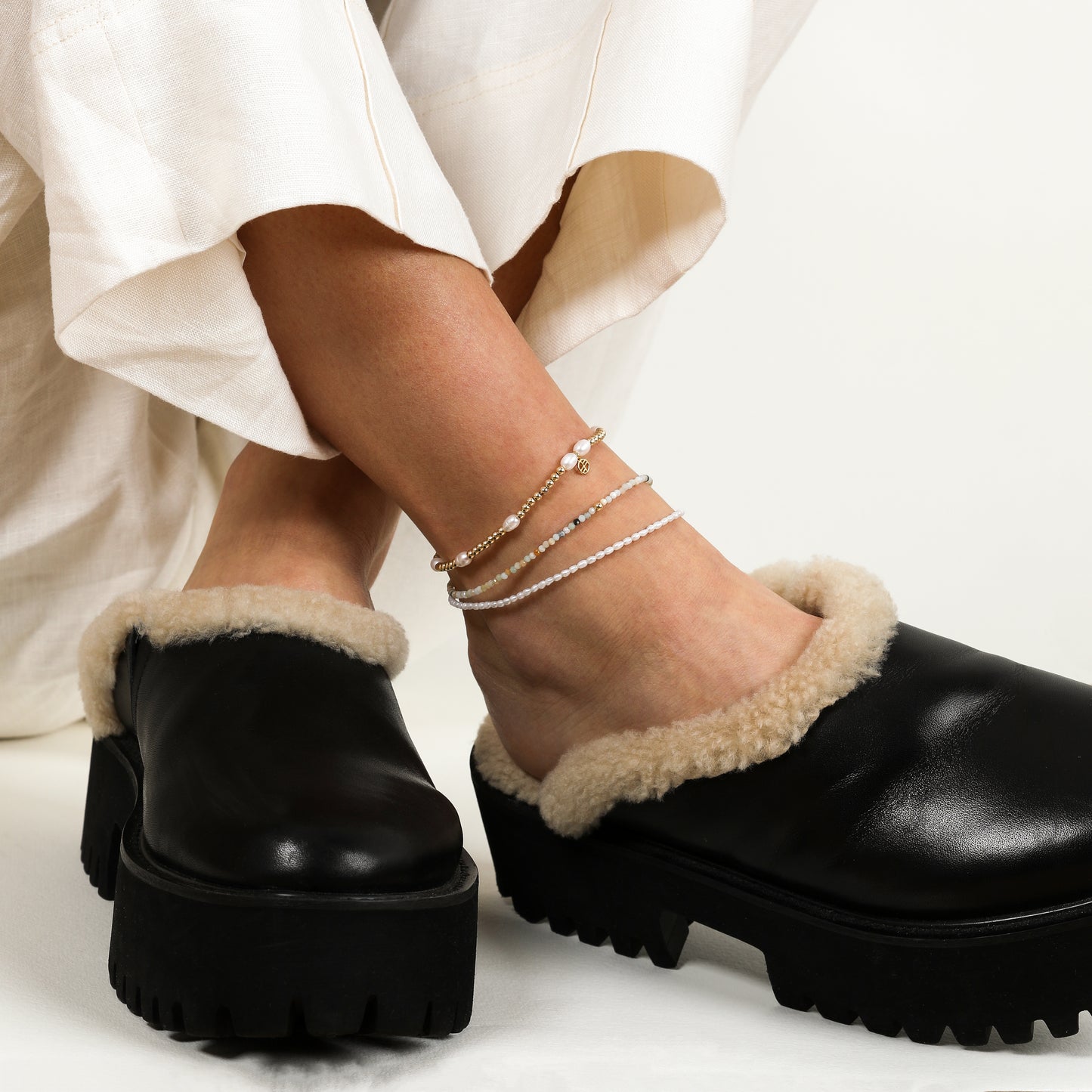 A coloured stretchy anklet with freshwater pearls and a small gold charm, worn on the ankle