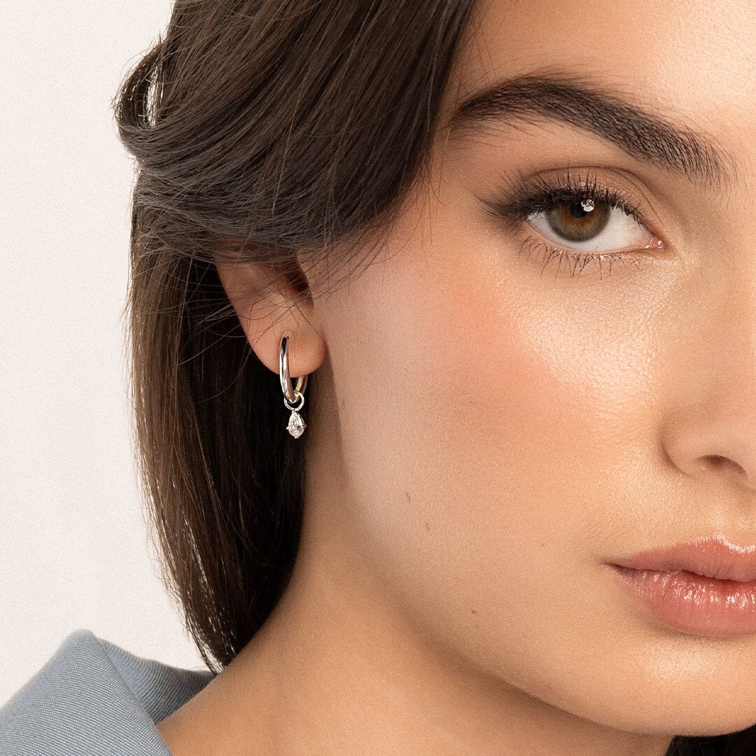 A pair of silver-colored hoop earrings with hoop charms, worn in models ears