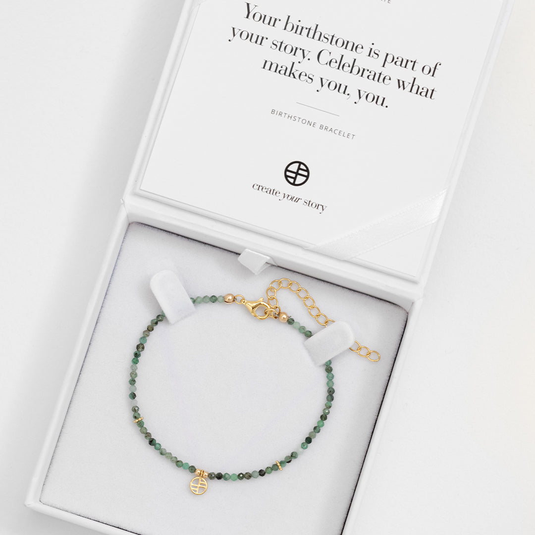 A beaded bracelet with green gemstones and a gold-tone clasp and charm, displayed in white box