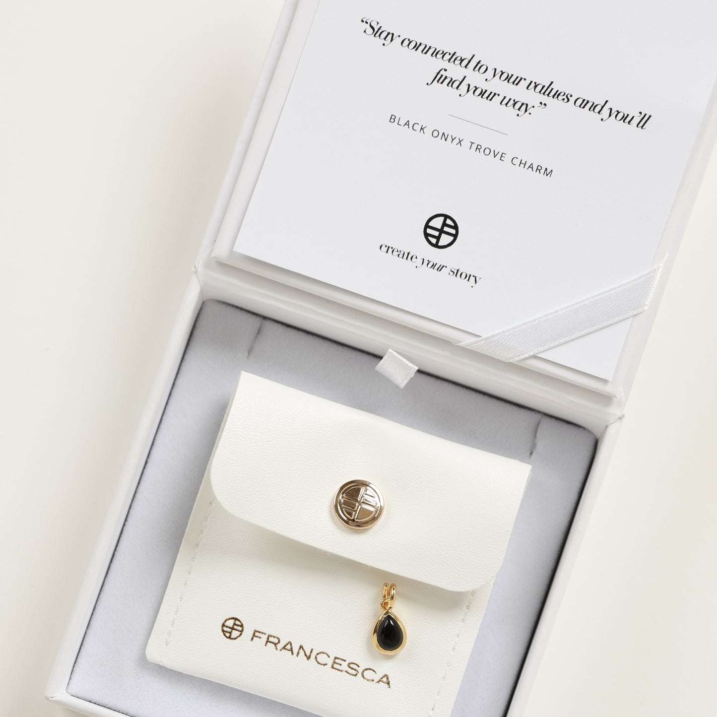 A gold charm with a teardrop-shaped black onyx stone in white box