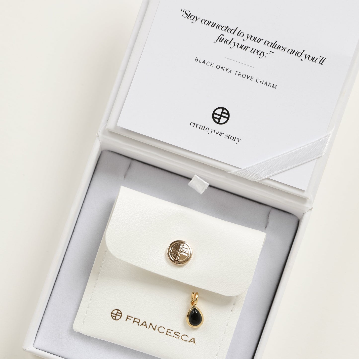 A gold charm with a teardrop-shaped black onyx stone in white box
