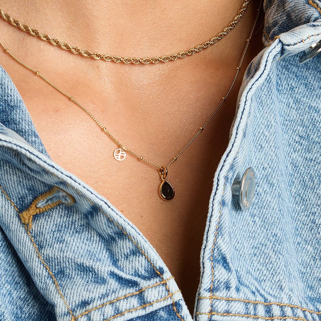 A gold charm with a teardrop-shaped black onyx stone on a chain, around the neck