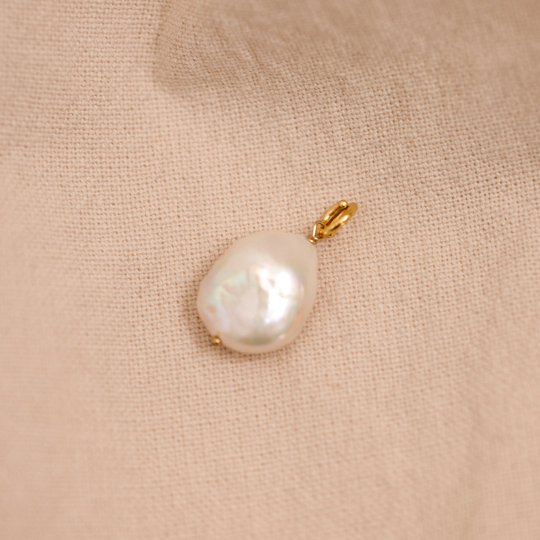 A medium sized pearl charm with gold findings, on beige background