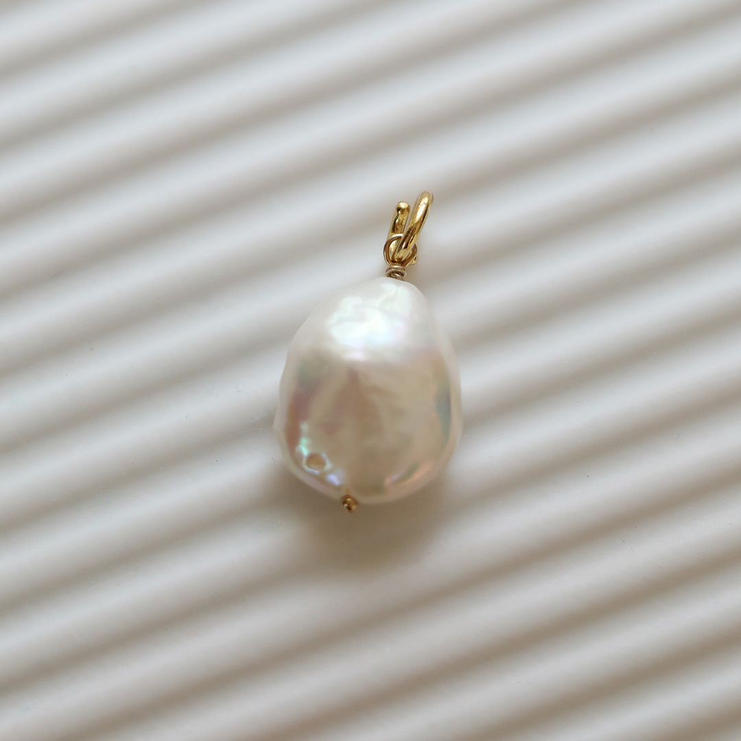 A medium sized pearl charm with gold findings, on white background