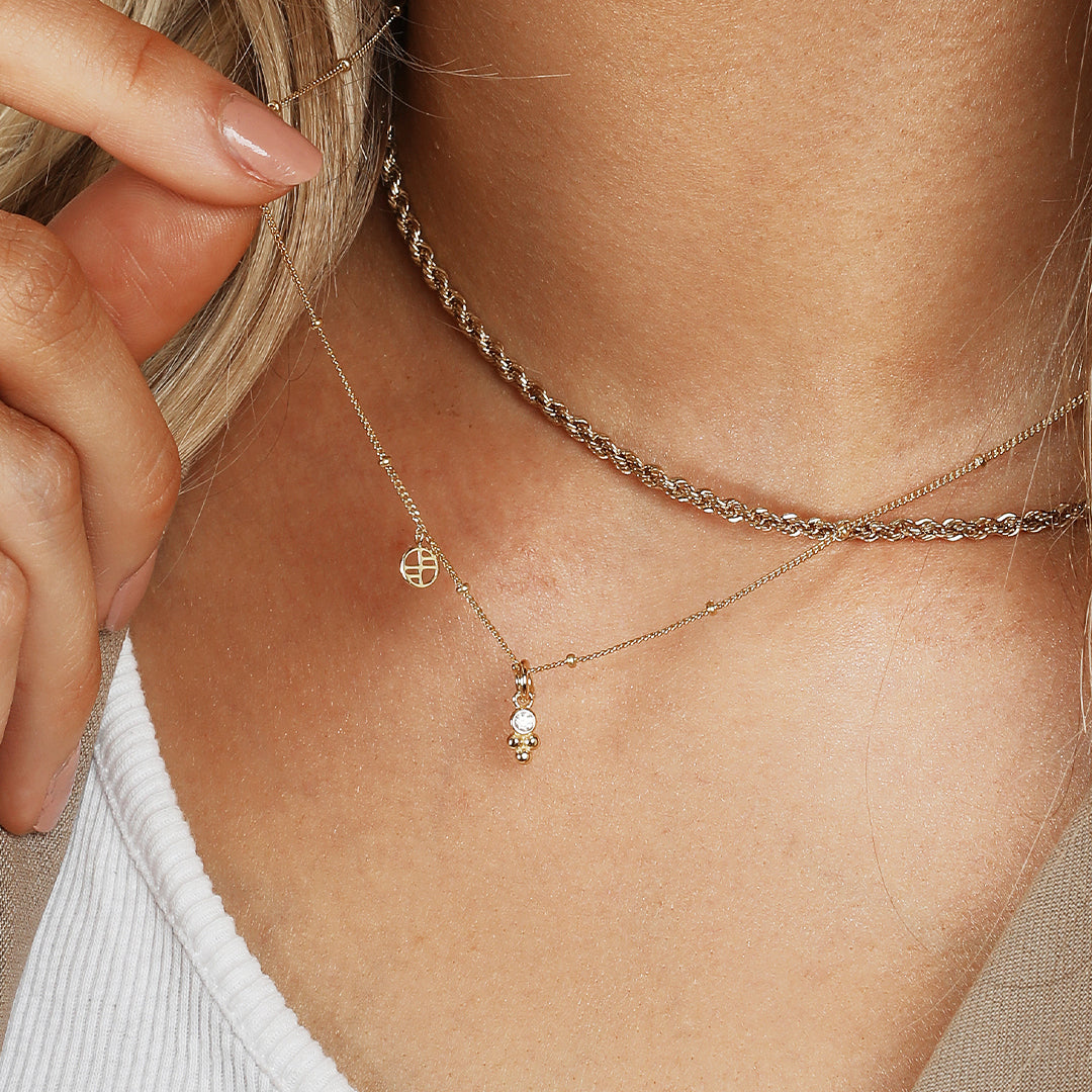 A small gold charm featuring a cubic zirconia and a floral design, attached to chain, on models neck