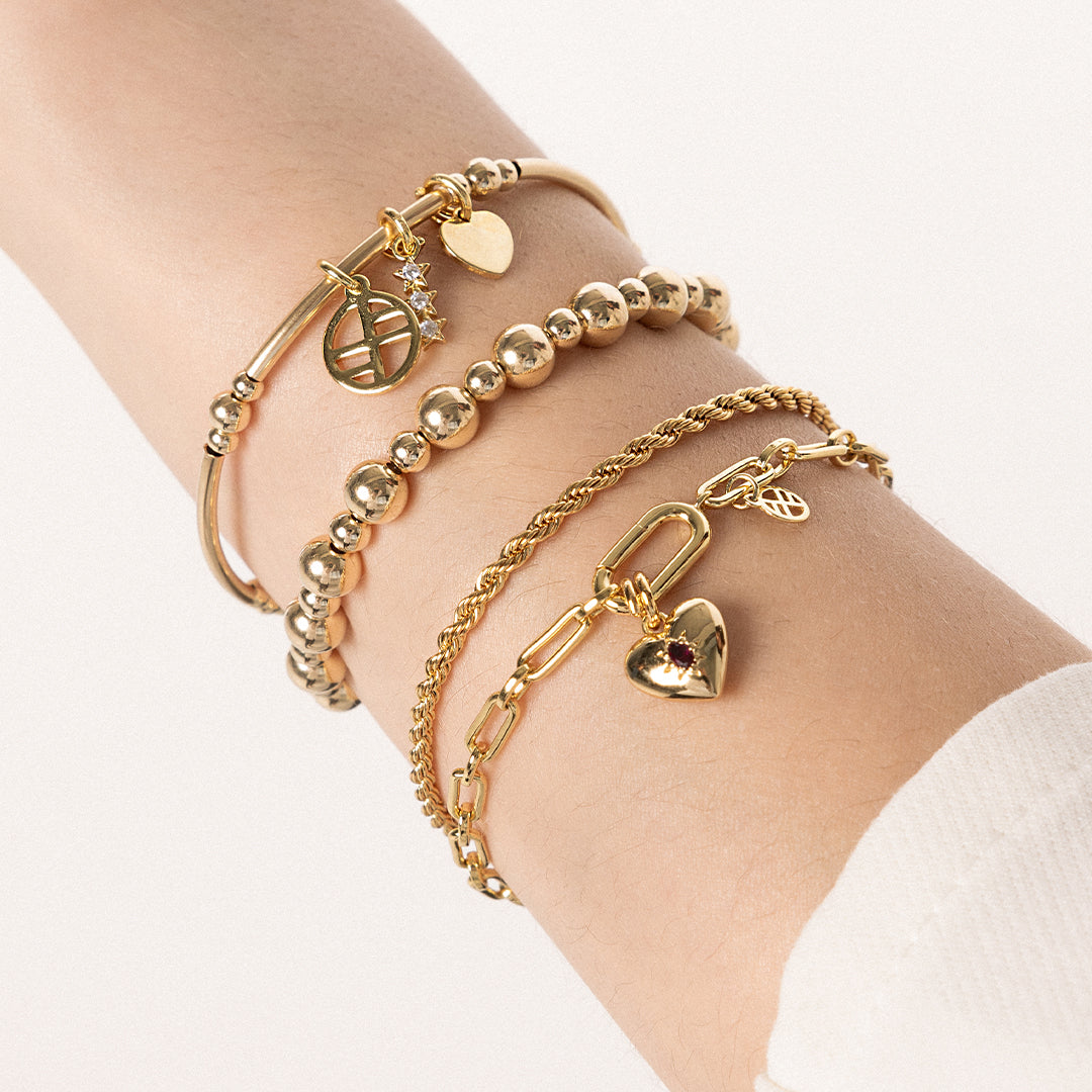 A gold-tone rope bracelet with a extender chain, layered with bracelets, on the wrist