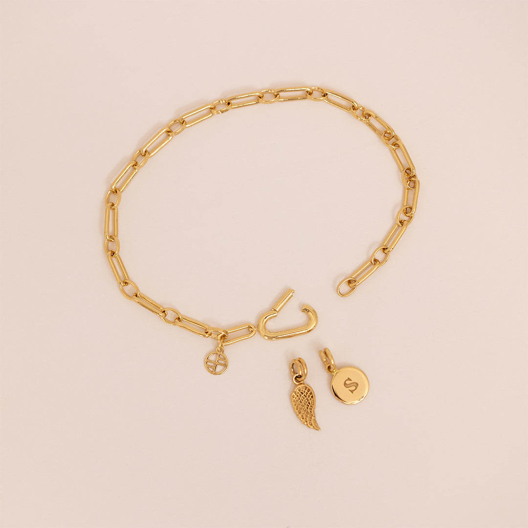 A gold-toned link bracelet, displayed on beige background, with the clasp opened