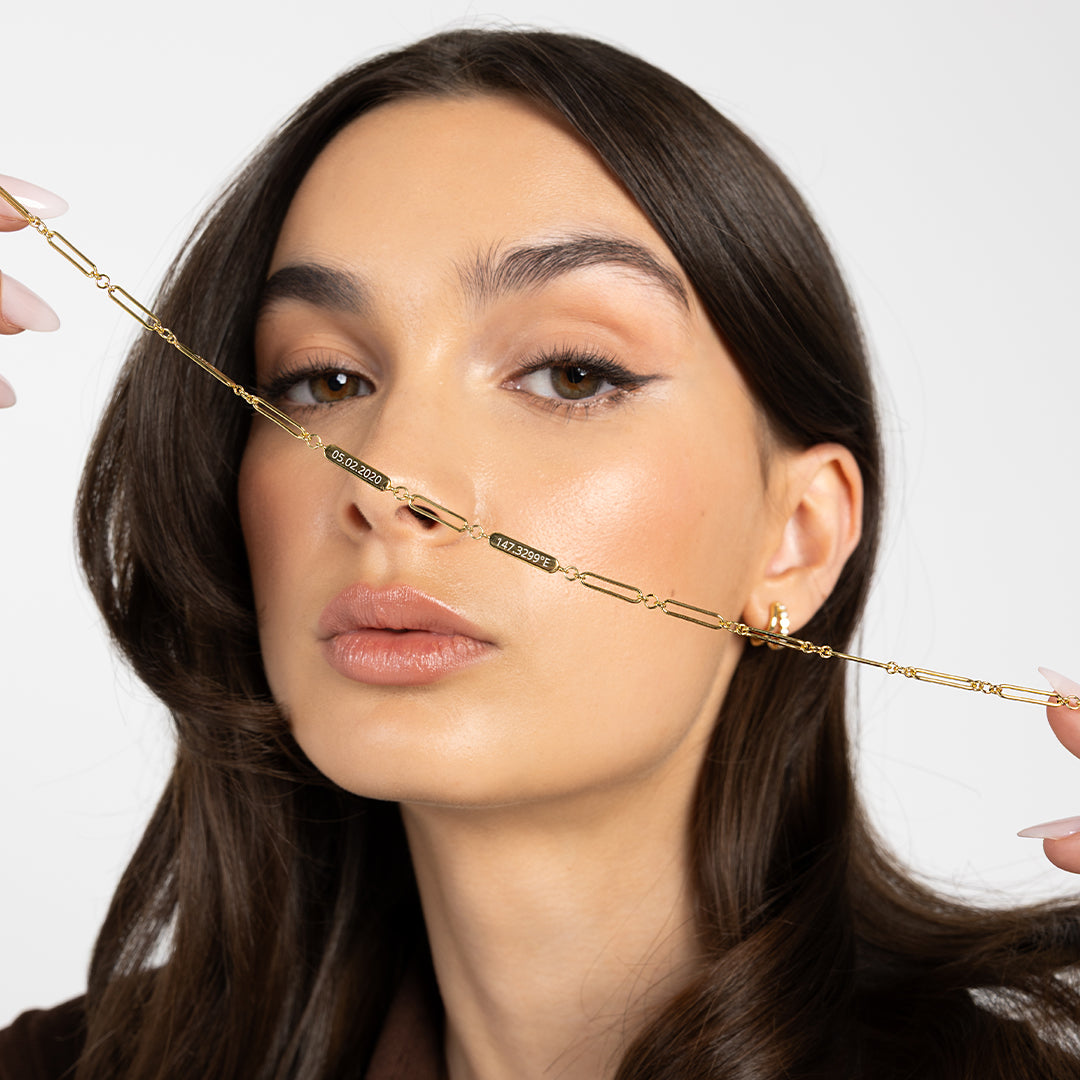 A gold chain necklace with two engraveable panels held up by model