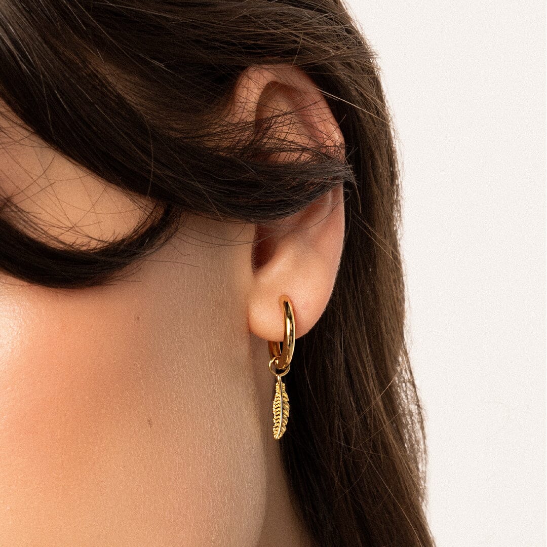 A set of two gold hoop charms with a feather design, on hoops, in the ear