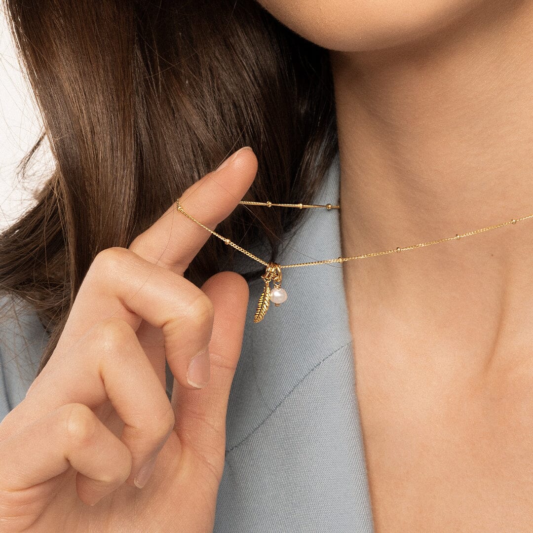 A petite pearl charm with gold findings, on a gold chain, worn by model