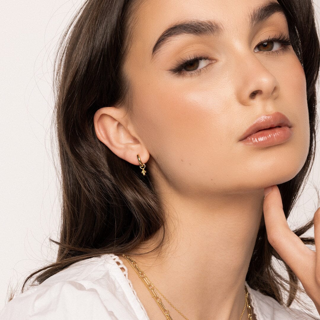 A pair of gold-tone hoop earrings with bobble details, worn in models ear