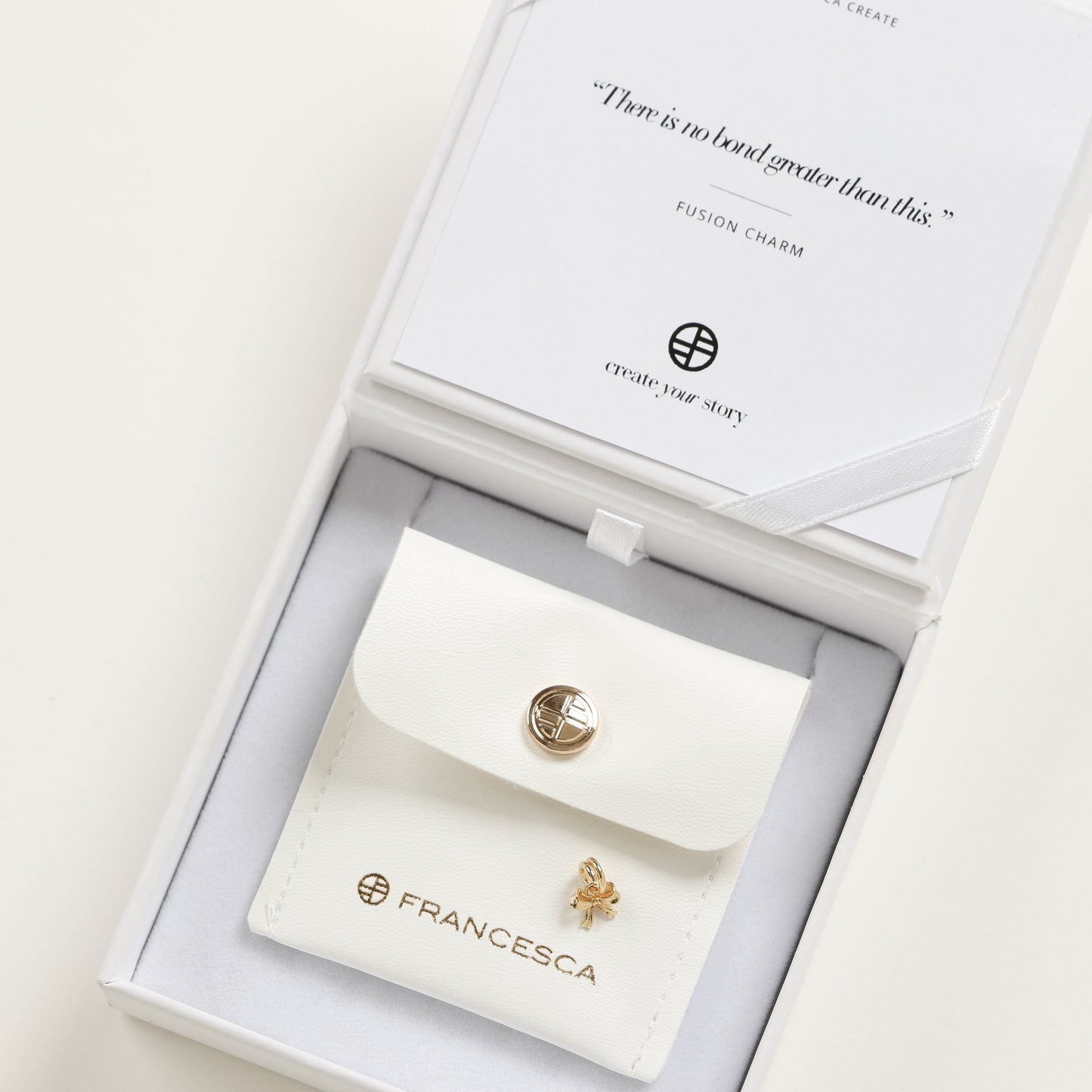 A small gold bow charm with a loop on top for attachment, displayed in a white box