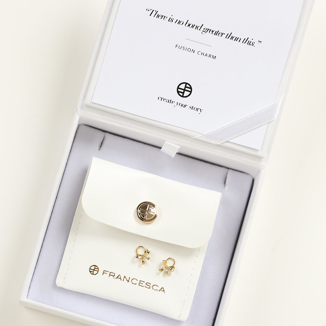 A set of two gold hoop charms with a bow design, in white box