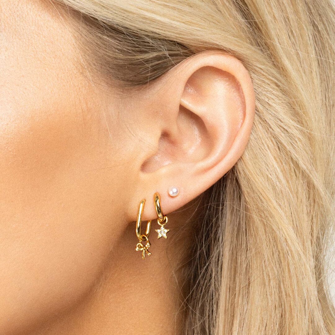 A set of two gold hoop charms with a bow design, on hoop, in ears