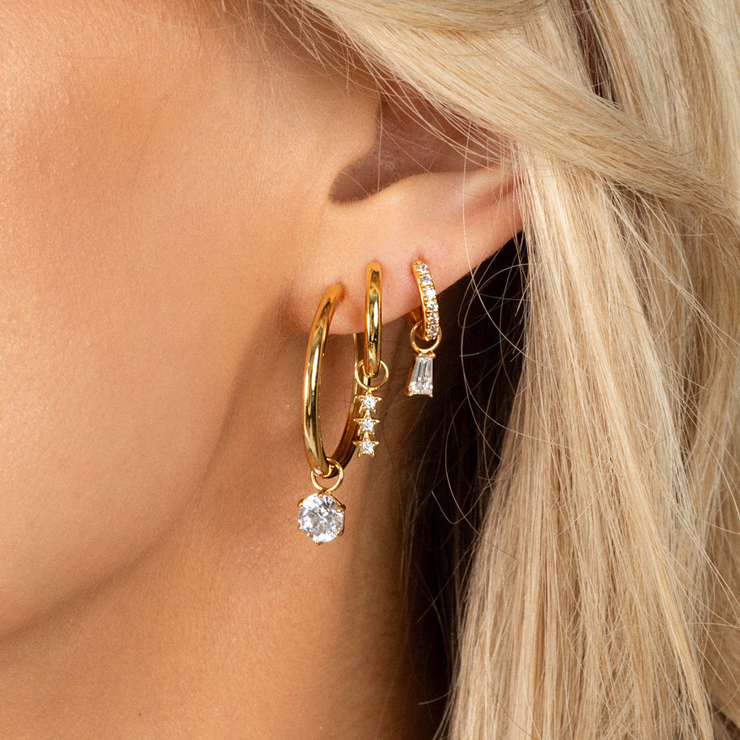 A set of two hoop charms with gold metal tone, designed to be attached to earrings, worn on hoops, in models ear