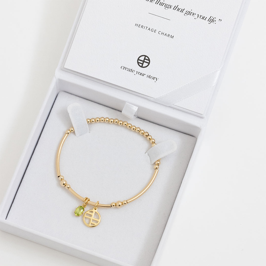 A gold-tone heritage charm bracelet with a beaded chain and a green oval charm, in white box