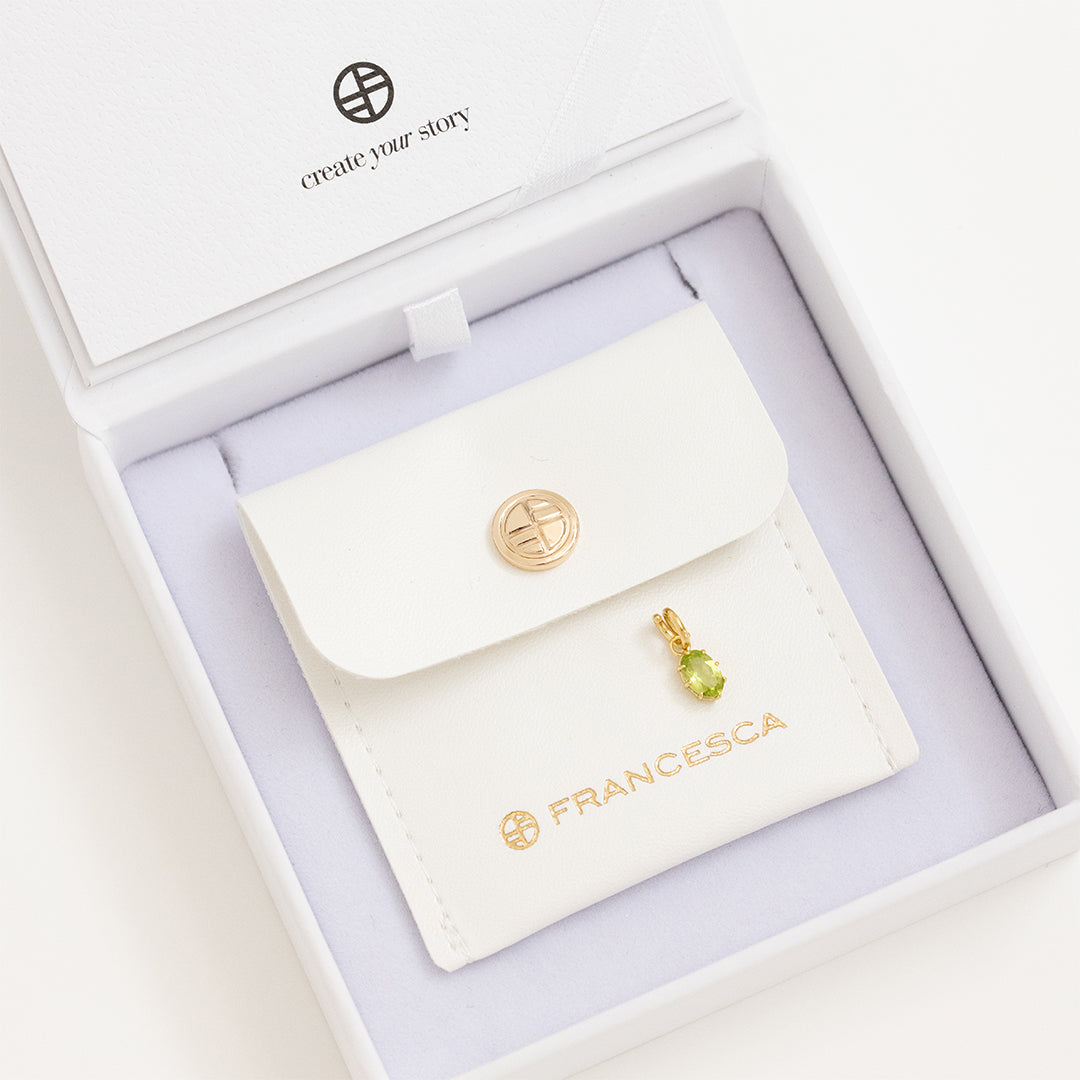A gold charm with an olive green cubic zirconia, displayed in white box