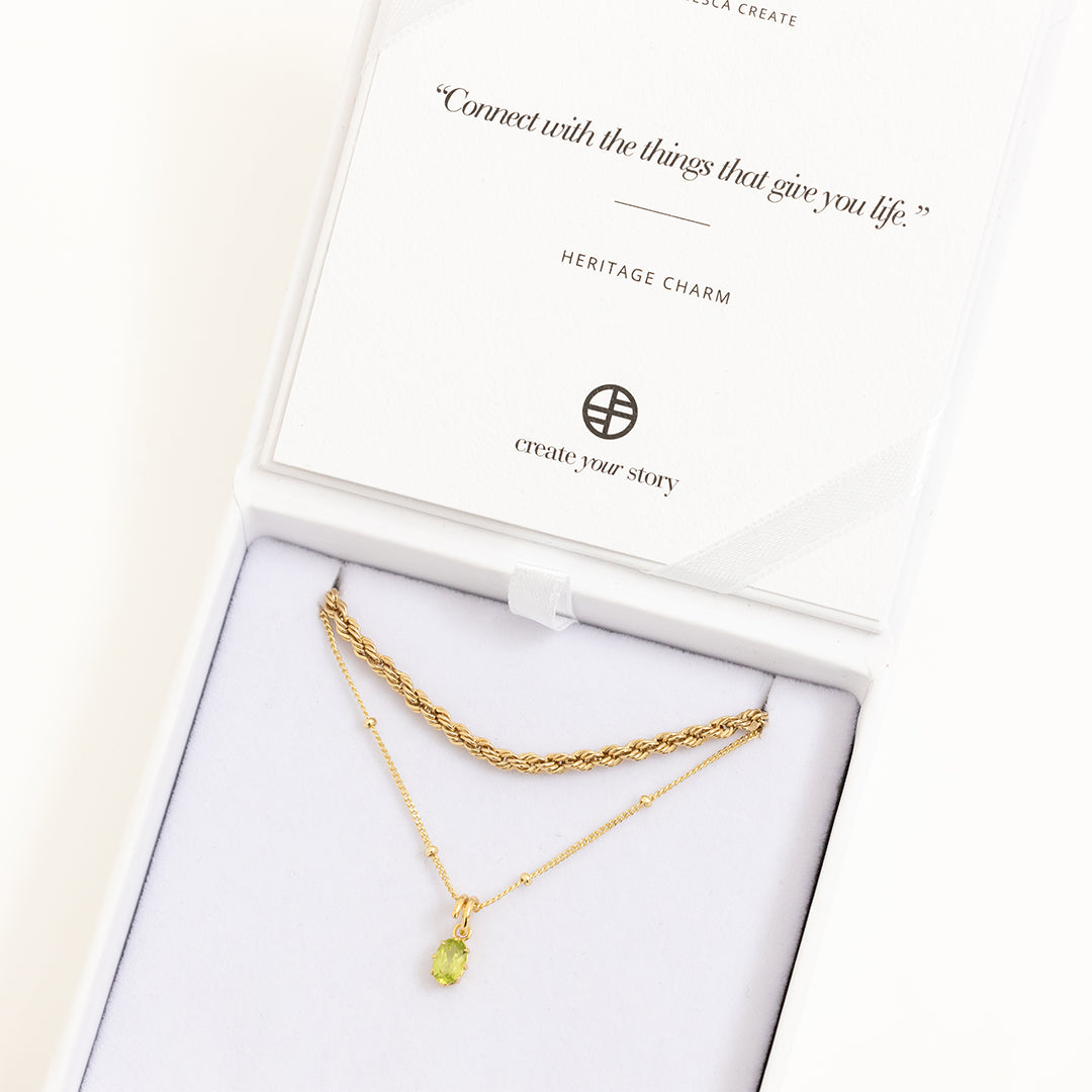 A green, oval-shaped charm pendant necklace with a gold metal chain, in white box