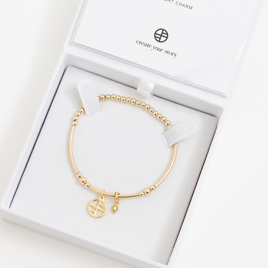 A gold-tone charm bracelet with a petite diamond charm and a stretchy bead chain, displayed in white box