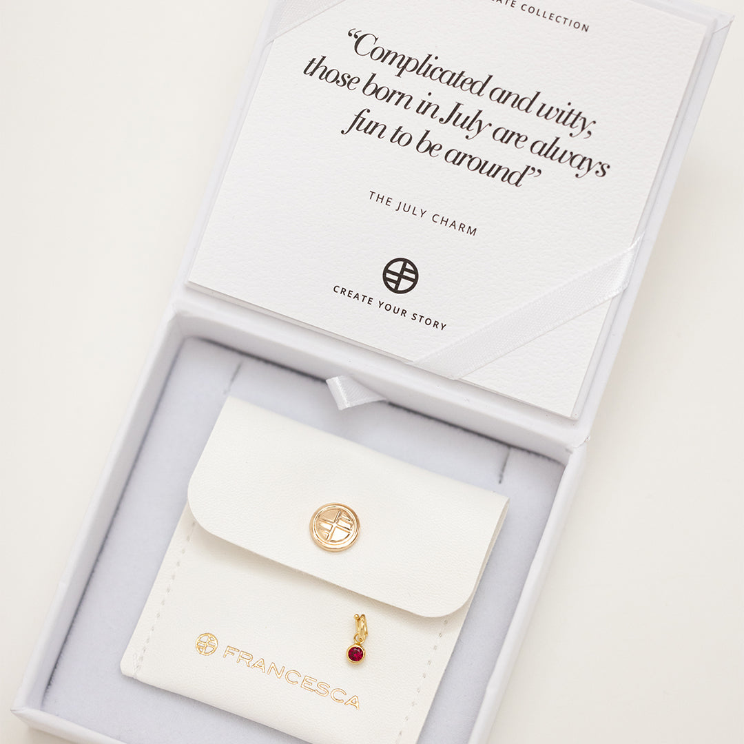 Round gold charm with bezel-set ruby cubic zirconia representing the July birthstone in white box