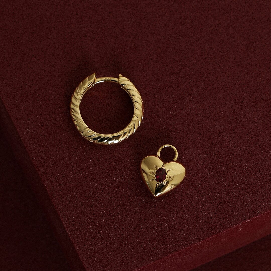 gold hoop charm with heart charms with deep red oval cubic zirconias next to gold hoop on red background