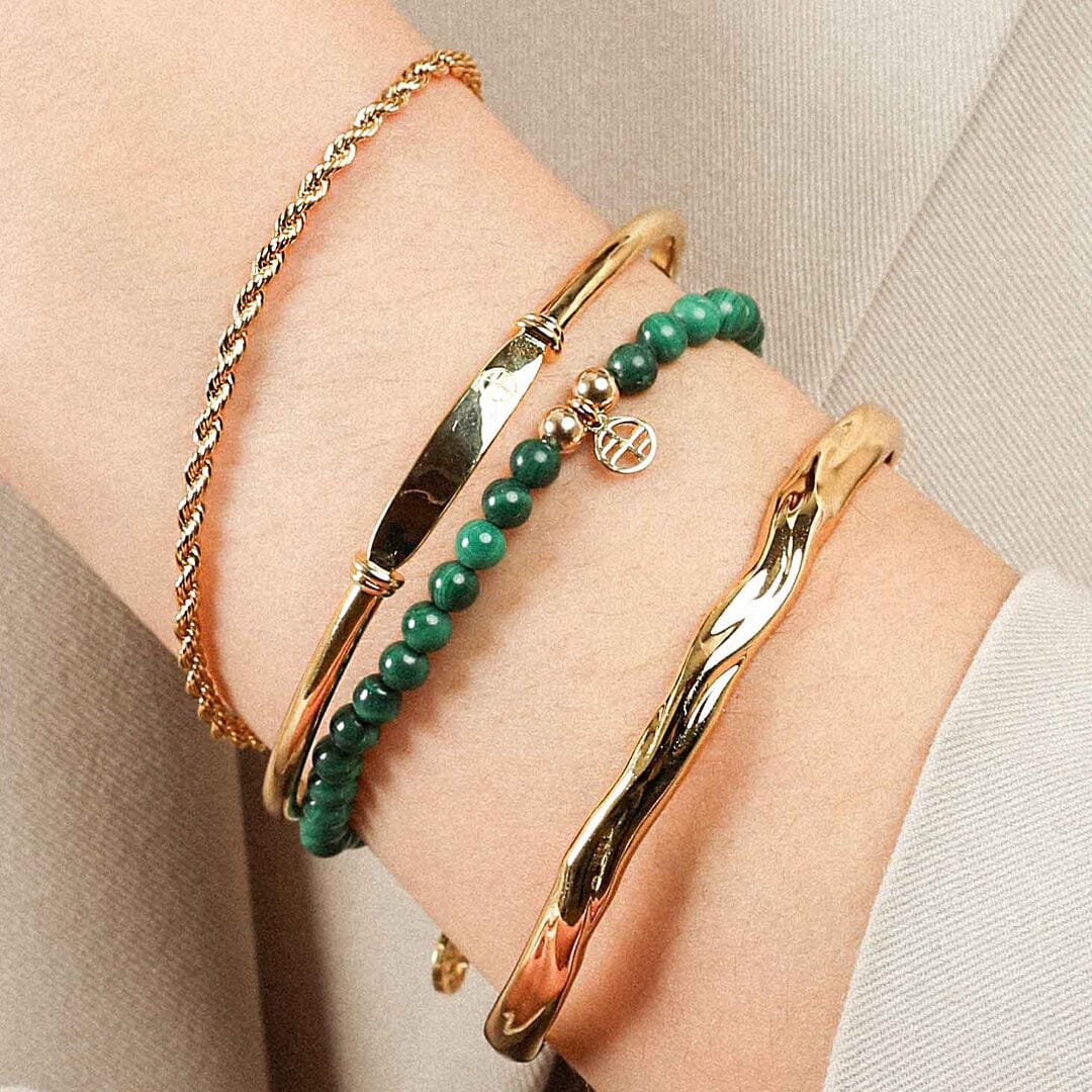 A beaded bracelet made of green malachite stones and metal beads with a gold-colored charm, on wrist
