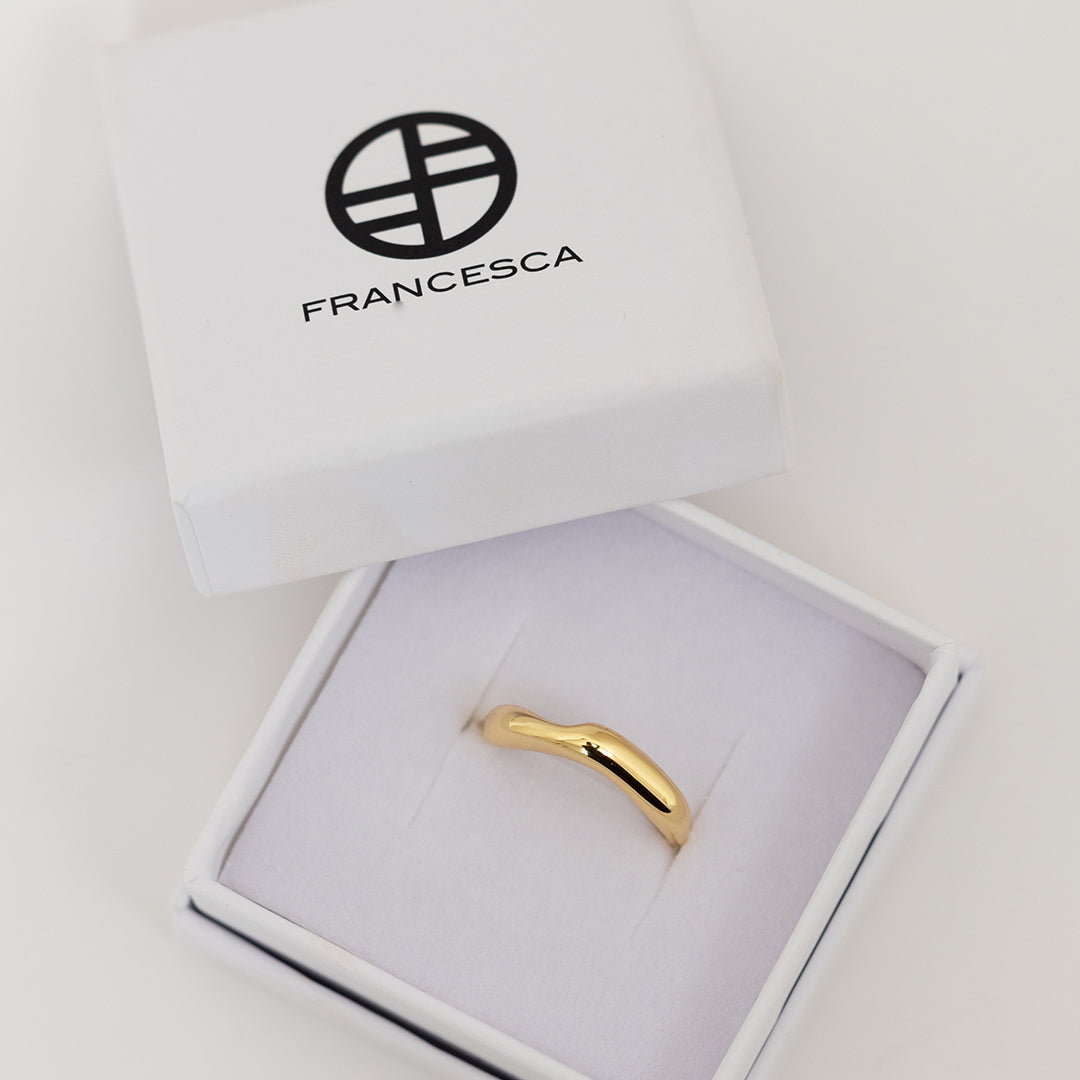 A gold-coloured ring with an irregular, smooth shape in a Francesca box