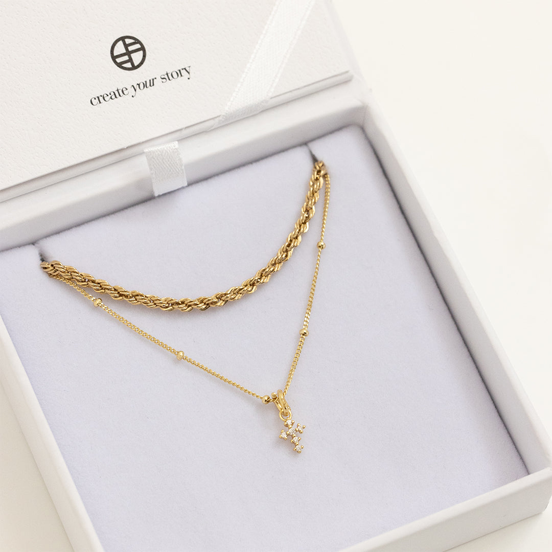 A gold-tone Nurture Cross Charm Pendant Necklace with a vintage cross shape on a chain, in white box