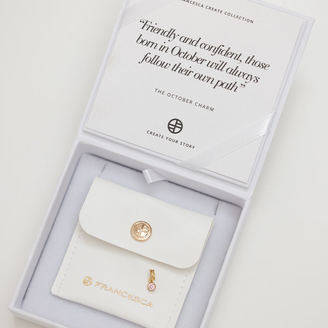 A round gold charm with a pink birthstone, designed for October birthdays displayed in box