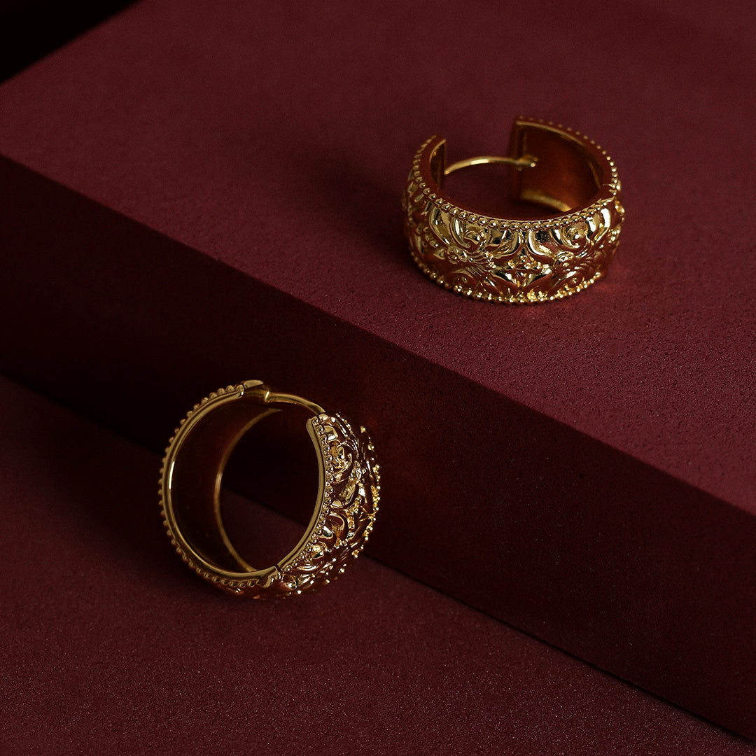 intricately designed statement gold hoops deep red background
