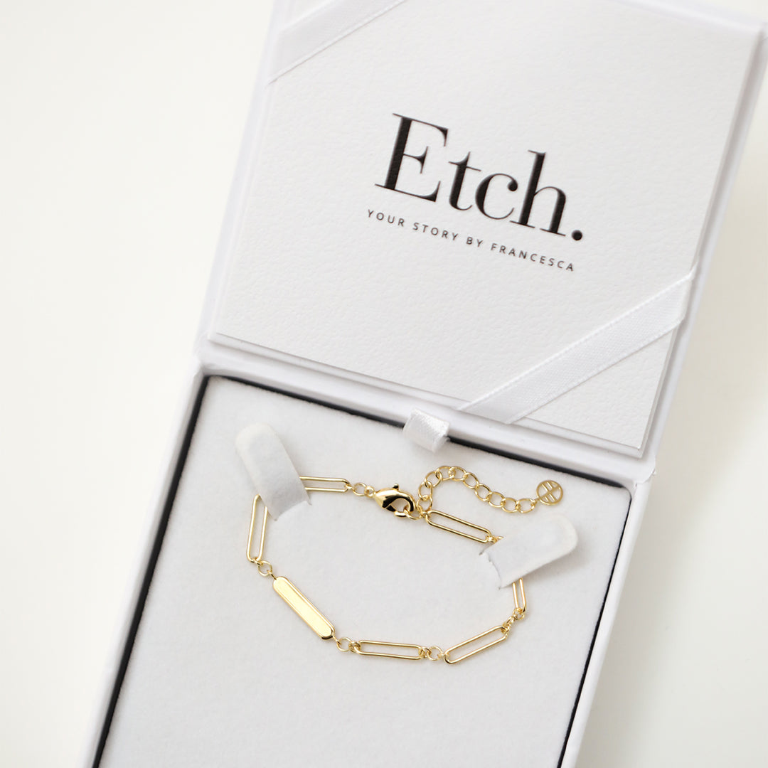 A gold-tone bracelet with a chain design and an engraving bar, displayed in a white box, made for children