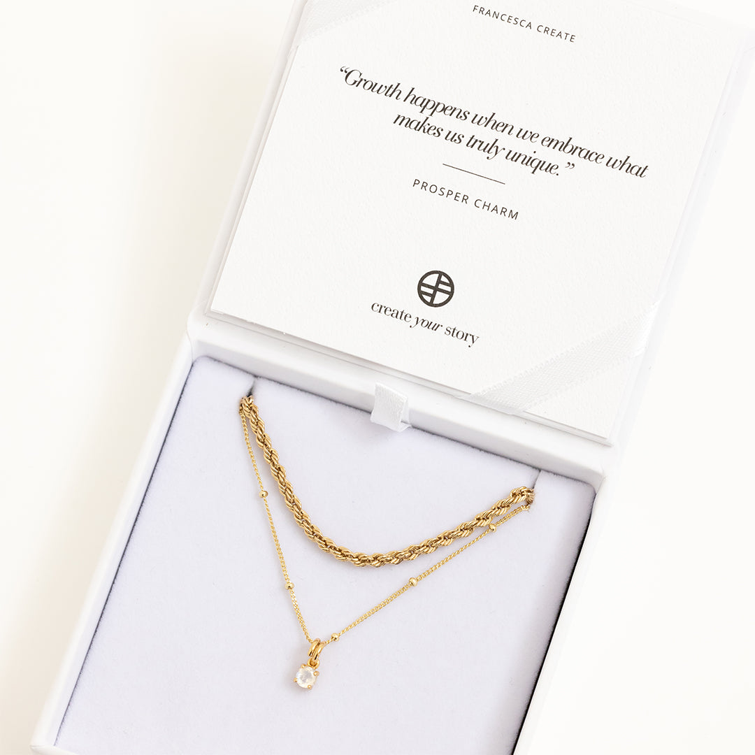 A gold-tone charm necklace with a small moonstone pendant, displayed in white box
