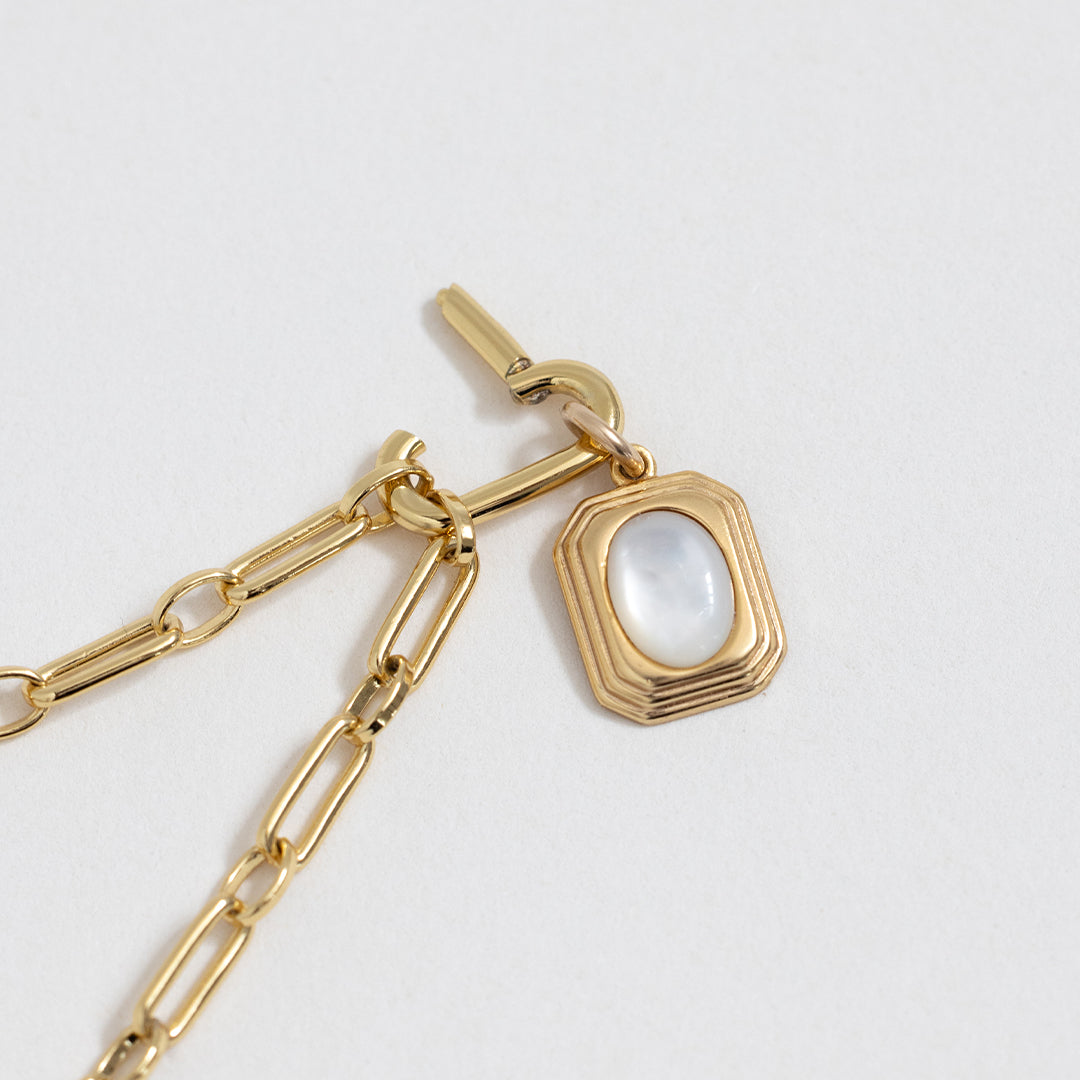 A gold-coloured pendant with an oval mother-of-pearl stone in the centre, on link chain, close up
