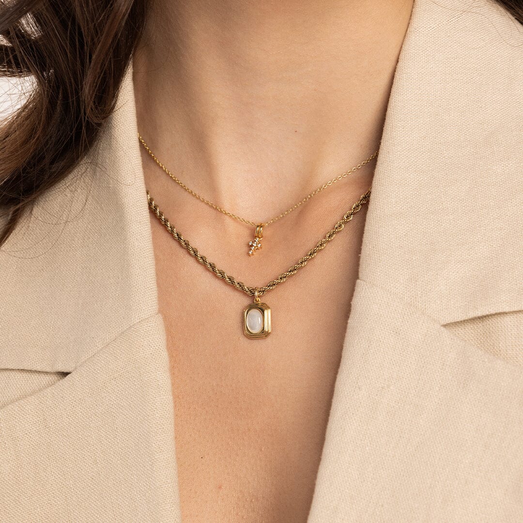 A gold-colored pendant with an oval mother-of-pearl stone in the center, on rope chain, worn on models neck