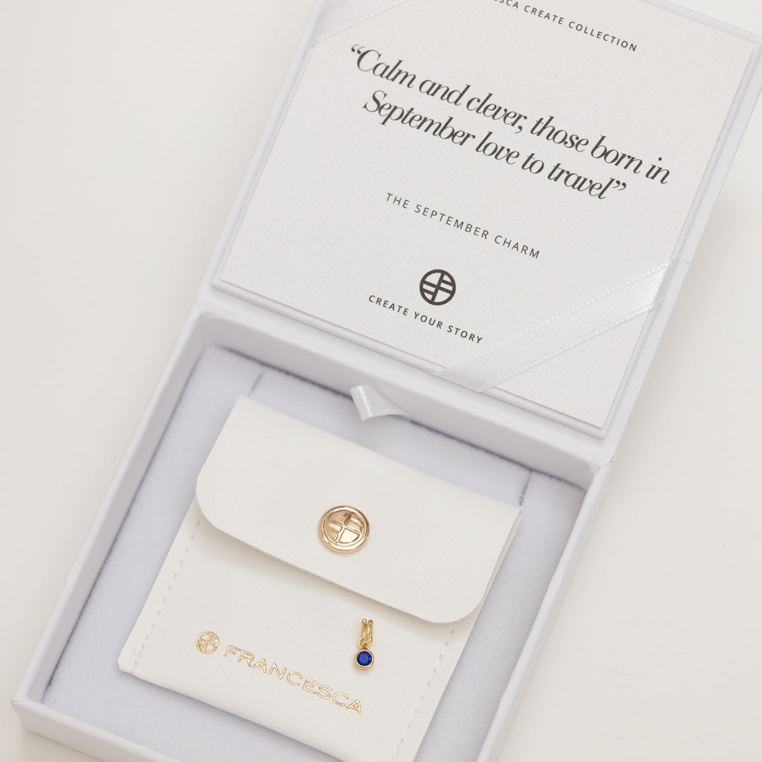 A round September birthstone charm with a blue cubic zirconia in box